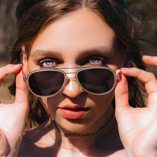 Close-up of a woman with blue eyes peering over a pair of silver-rimmed aviator sunglasses.