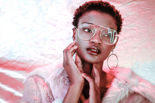 Woman with short hair, large glasses, and hoop earrings posing in a fur coat.