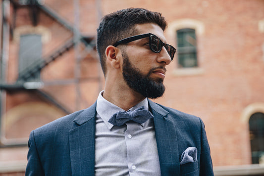 A bearded man in a blue suit and bow tie wearing classic black-framed sunglasses.