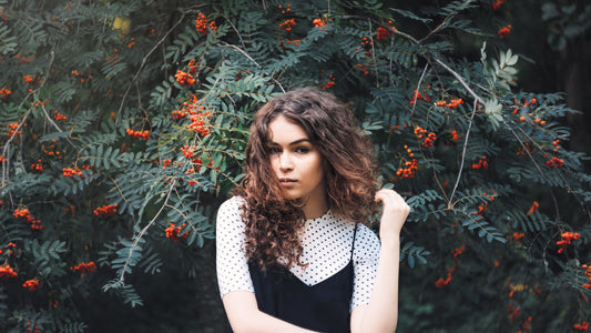 A young woman with curly hair posing in front of a tree with red berries.